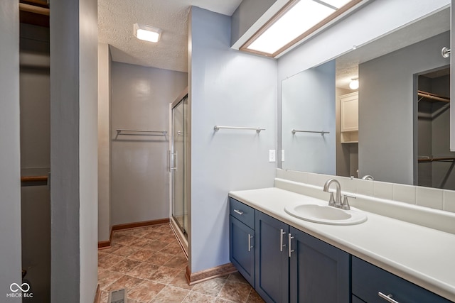 full bath featuring visible vents, a textured ceiling, a shower stall, vanity, and baseboards