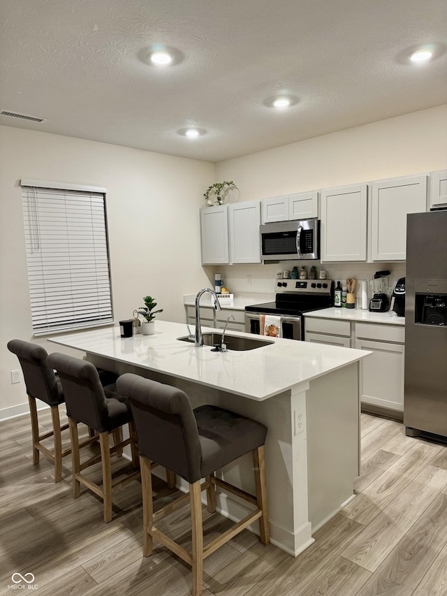 kitchen with an island with sink, a kitchen breakfast bar, stainless steel appliances, white cabinetry, and a sink