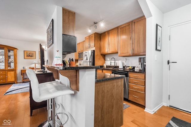 kitchen with appliances with stainless steel finishes, a kitchen bar, light wood-style flooring, and brown cabinets