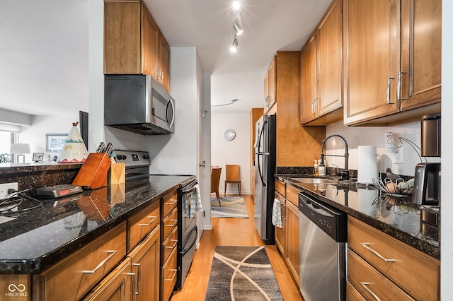 kitchen featuring appliances with stainless steel finishes, light wood-style floors, brown cabinetry, and a sink