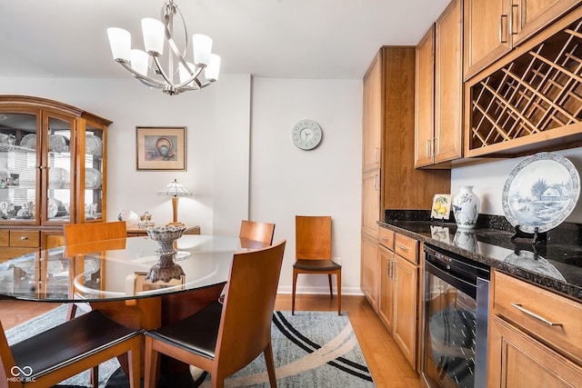 kitchen with beverage cooler, light wood-style floors, dark stone counters, brown cabinetry, and decorative light fixtures