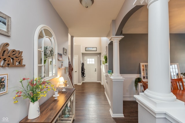 entryway featuring arched walkways, baseboards, stairway, dark wood-style floors, and ornate columns