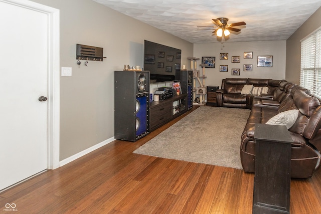 living area featuring dark wood-style floors, a textured ceiling, baseboards, and a ceiling fan