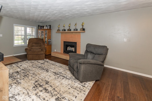 living area with dark wood-type flooring, a tile fireplace, a textured ceiling, and baseboards