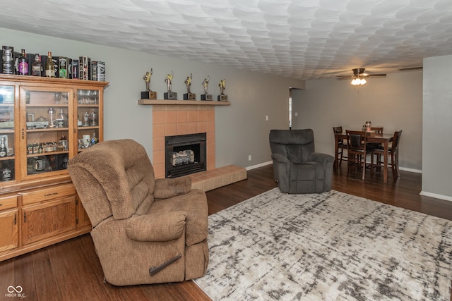 living room with a textured ceiling, a ceiling fan, baseboards, dark wood-style floors, and a tiled fireplace