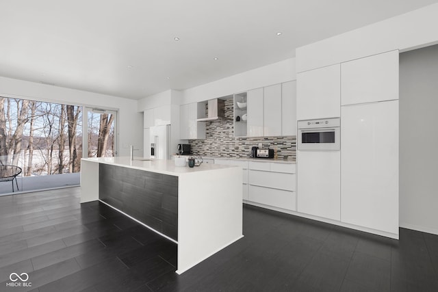 kitchen with white cabinets, light countertops, white oven, an island with sink, and modern cabinets