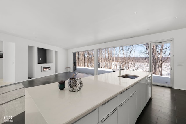 kitchen with a glass covered fireplace, an island with sink, modern cabinets, light countertops, and white cabinetry