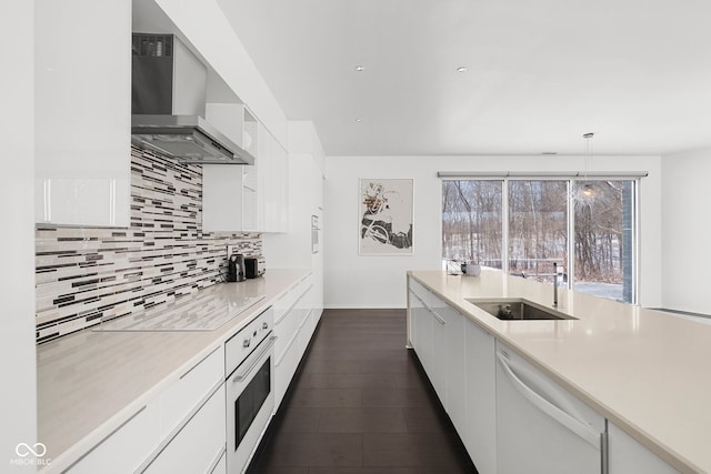 kitchen featuring white appliances, white cabinets, light countertops, wall chimney range hood, and decorative light fixtures