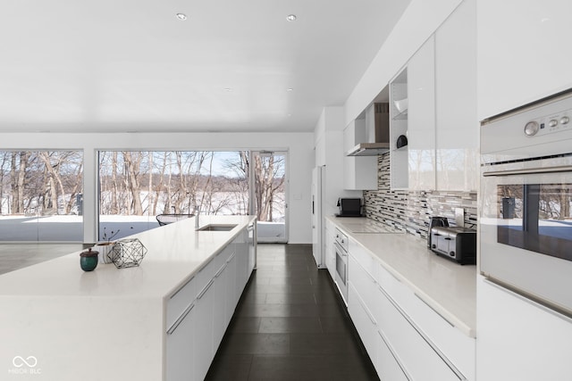 kitchen with light countertops, wall chimney range hood, modern cabinets, and white cabinetry