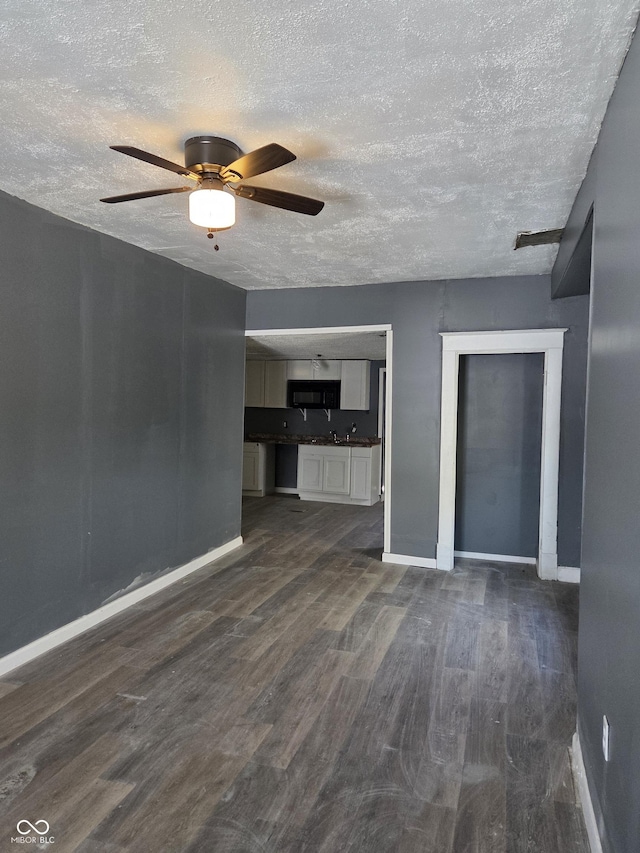 unfurnished living room with dark wood-type flooring, ceiling fan, a textured ceiling, and baseboards