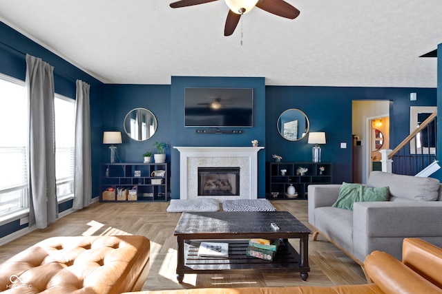 living room with a textured ceiling, ceiling fan, a glass covered fireplace, and stairs