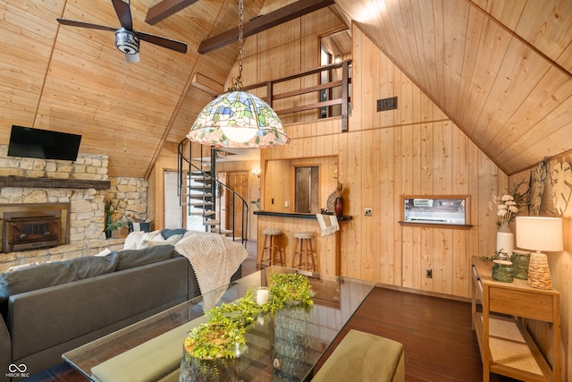 living area featuring stairway, wood ceiling, wood walls, a stone fireplace, and wood finished floors