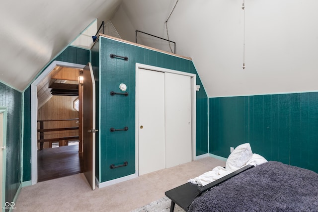 carpeted bedroom with wood walls, vaulted ceiling, and a closet