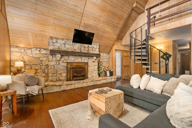 living room featuring wooden walls, wood ceiling, hardwood / wood-style floors, stairs, and a stone fireplace