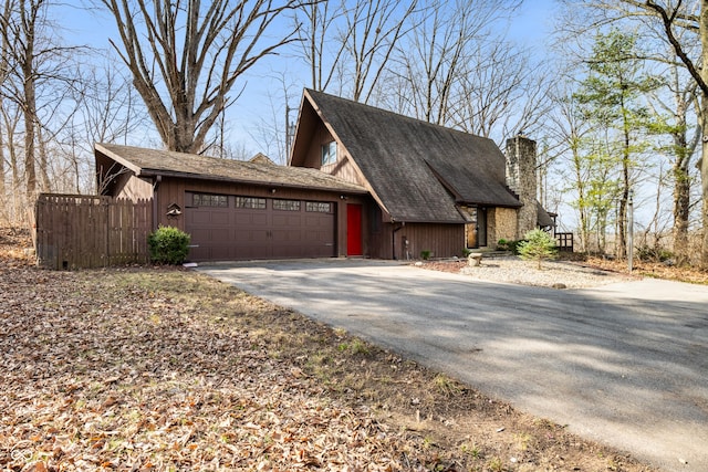 view of side of property featuring a garage, aphalt driveway, a chimney, and fence