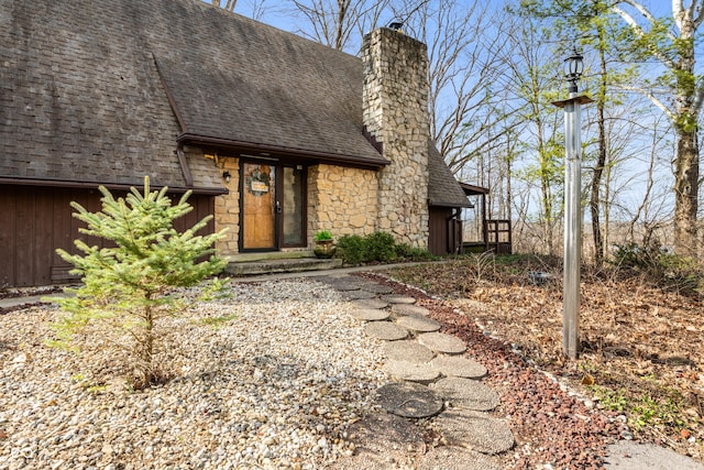 view of front of home with stone siding, roof with shingles, a chimney, and board and batten siding