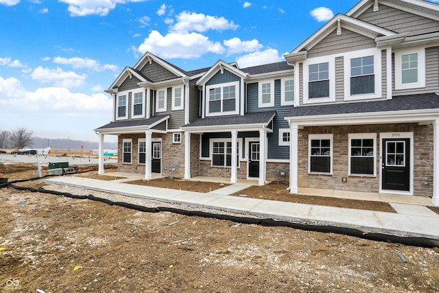 multi unit property featuring stone siding, covered porch, and roof with shingles