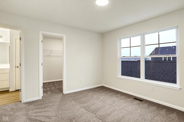 unfurnished bedroom with visible vents, a walk in closet, baseboards, carpet, and a closet