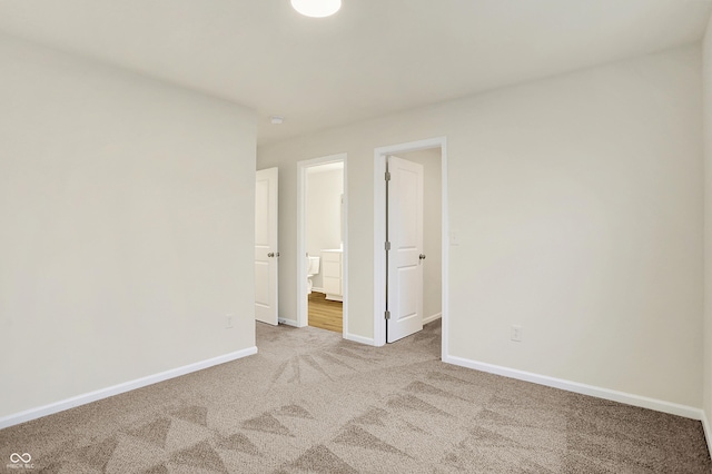 unfurnished bedroom featuring light colored carpet, ensuite bathroom, and baseboards