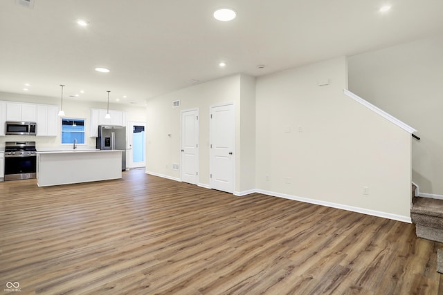 unfurnished living room with light wood-type flooring, a sink, recessed lighting, baseboards, and stairs