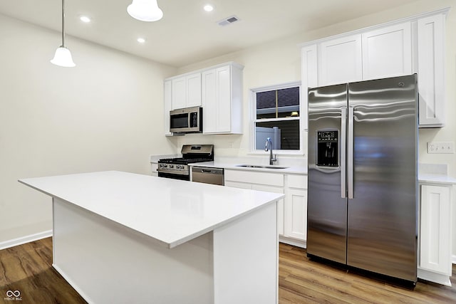 kitchen with a center island, light countertops, wood finished floors, stainless steel appliances, and a sink