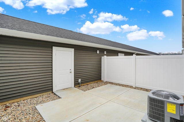 property entrance featuring central air condition unit, a patio area, fence, and roof with shingles