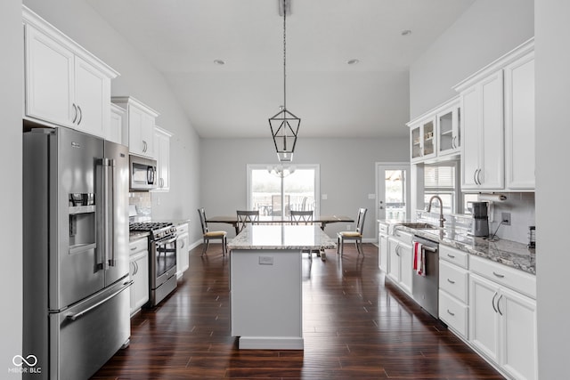 kitchen with white cabinets, a kitchen island, glass insert cabinets, light stone countertops, and stainless steel appliances