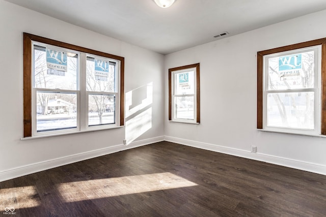 spare room with baseboards, dark wood-style flooring, and visible vents