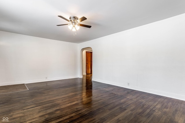 empty room with arched walkways, baseboards, dark wood-style floors, and ceiling fan