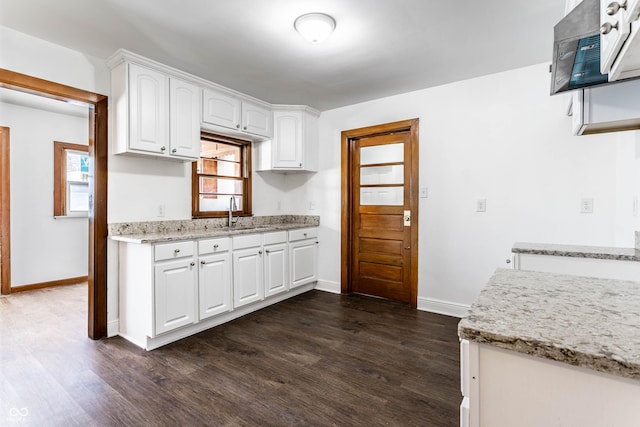 kitchen featuring light stone counters, a sink, dark wood-style flooring, baseboards, and white cabinetry