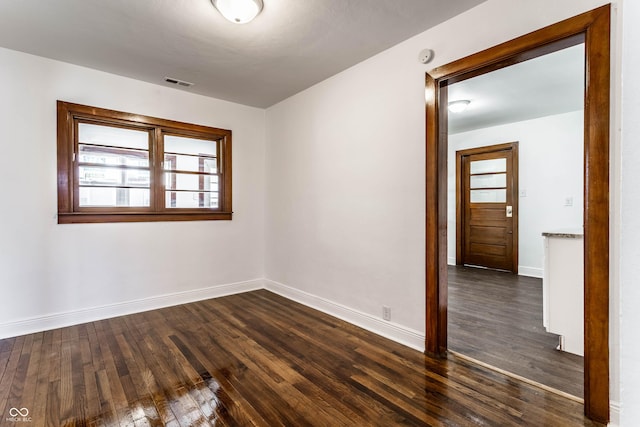 empty room featuring visible vents, baseboards, and dark wood-style flooring
