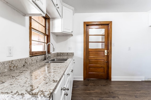 kitchen with light stone counters, a sink, baseboards, white cabinetry, and dark wood-style floors