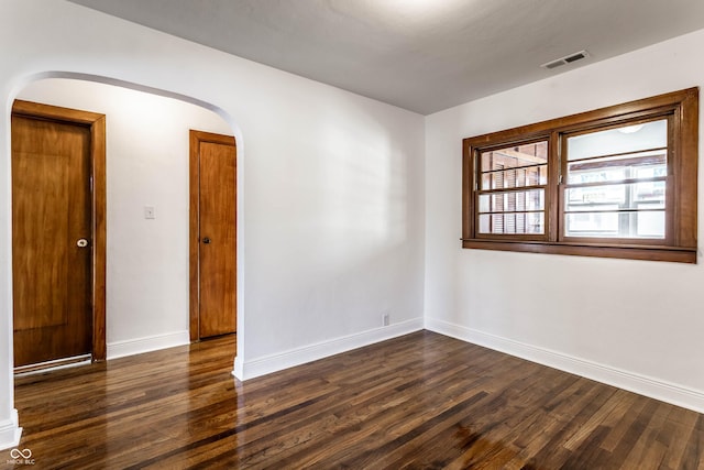 spare room with baseboards, visible vents, arched walkways, and dark wood-style floors
