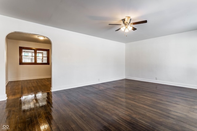 empty room with arched walkways, dark wood finished floors, baseboards, and ceiling fan