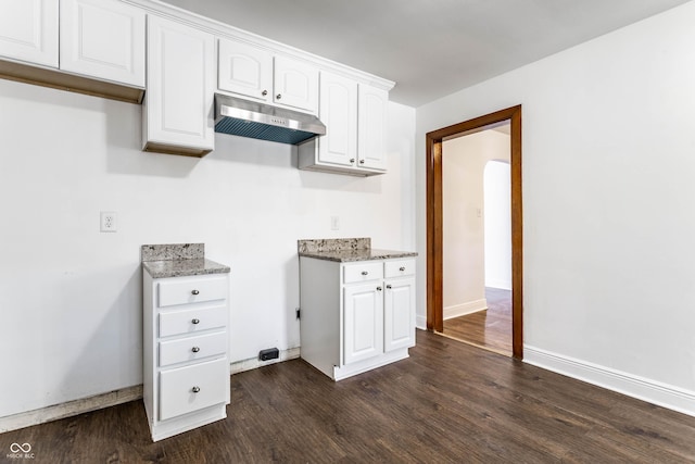 kitchen with light stone counters, under cabinet range hood, arched walkways, white cabinets, and dark wood-style flooring