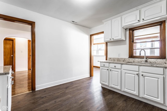 kitchen with arched walkways, dark wood-style flooring, a sink, and white cabinetry