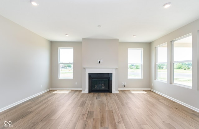 unfurnished living room with baseboards, recessed lighting, a glass covered fireplace, and light wood-style floors