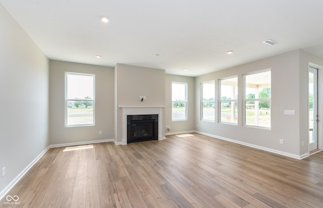 unfurnished living room featuring light wood-style floors, baseboards, visible vents, and a glass covered fireplace