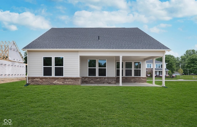 rear view of property featuring a yard, brick siding, a patio area, and a shingled roof