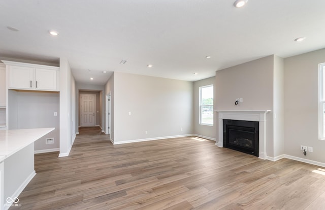 unfurnished living room featuring baseboards, recessed lighting, a fireplace, and light wood-style floors