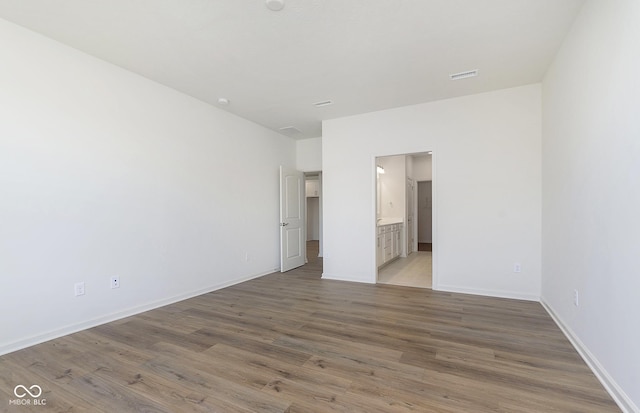 unfurnished bedroom featuring baseboards, connected bathroom, visible vents, and wood finished floors