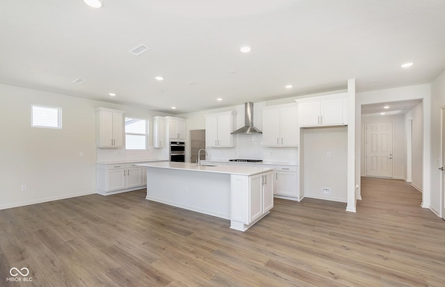 kitchen featuring light wood-type flooring, wall chimney range hood, white cabinets, and a sink