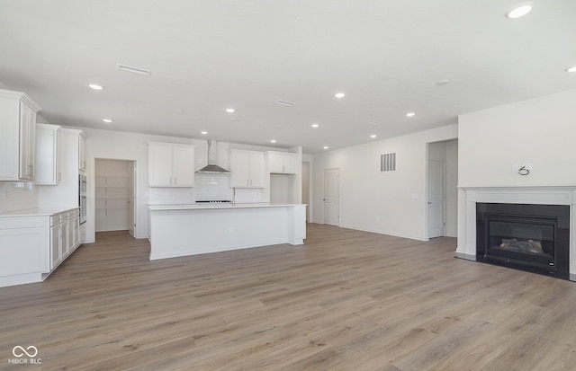 kitchen with tasteful backsplash, visible vents, open floor plan, light wood-type flooring, and wall chimney range hood