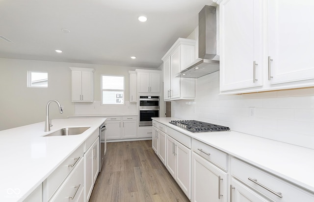 kitchen with a healthy amount of sunlight, wall chimney exhaust hood, appliances with stainless steel finishes, and a sink