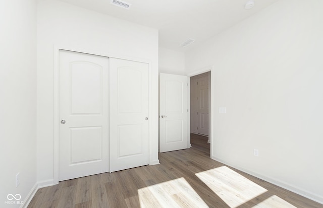 unfurnished bedroom featuring baseboards, a closet, visible vents, and wood finished floors