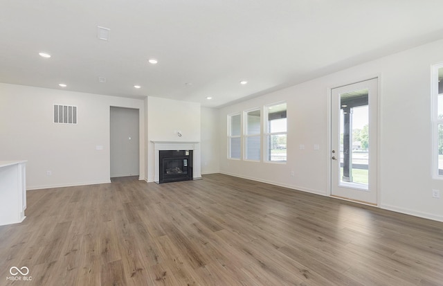 unfurnished living room with recessed lighting, visible vents, baseboards, light wood finished floors, and a glass covered fireplace