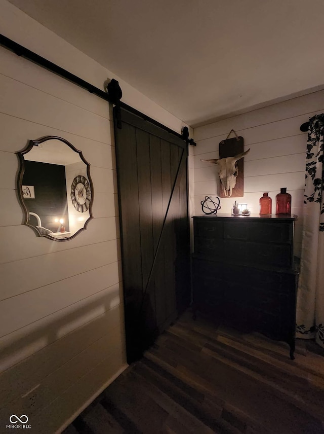 hallway featuring a barn door, wooden walls, and dark wood-type flooring