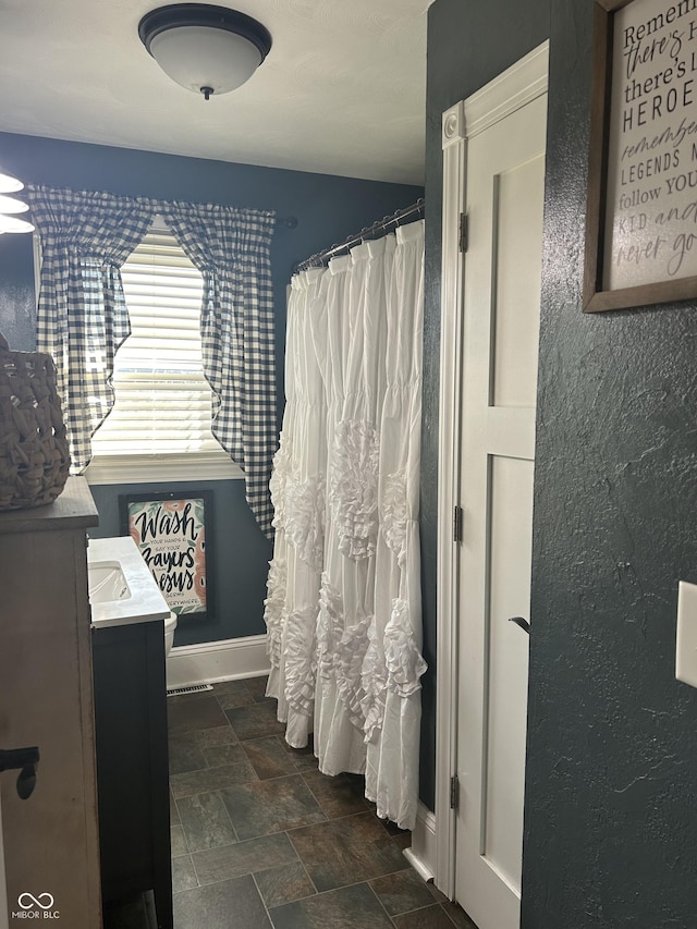 bathroom with a shower with curtain, stone finish floor, vanity, and baseboards