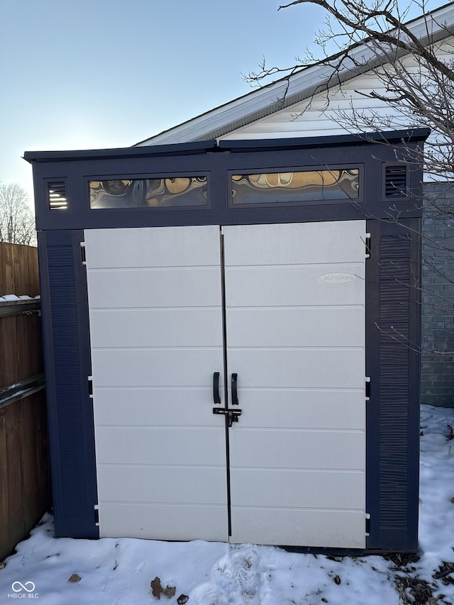 snow covered gate with an outdoor structure, fence, and a storage shed