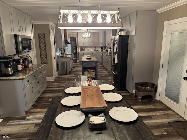 kitchen with dark wood finished floors, stainless steel microwave, decorative backsplash, ornamental molding, and freestanding refrigerator